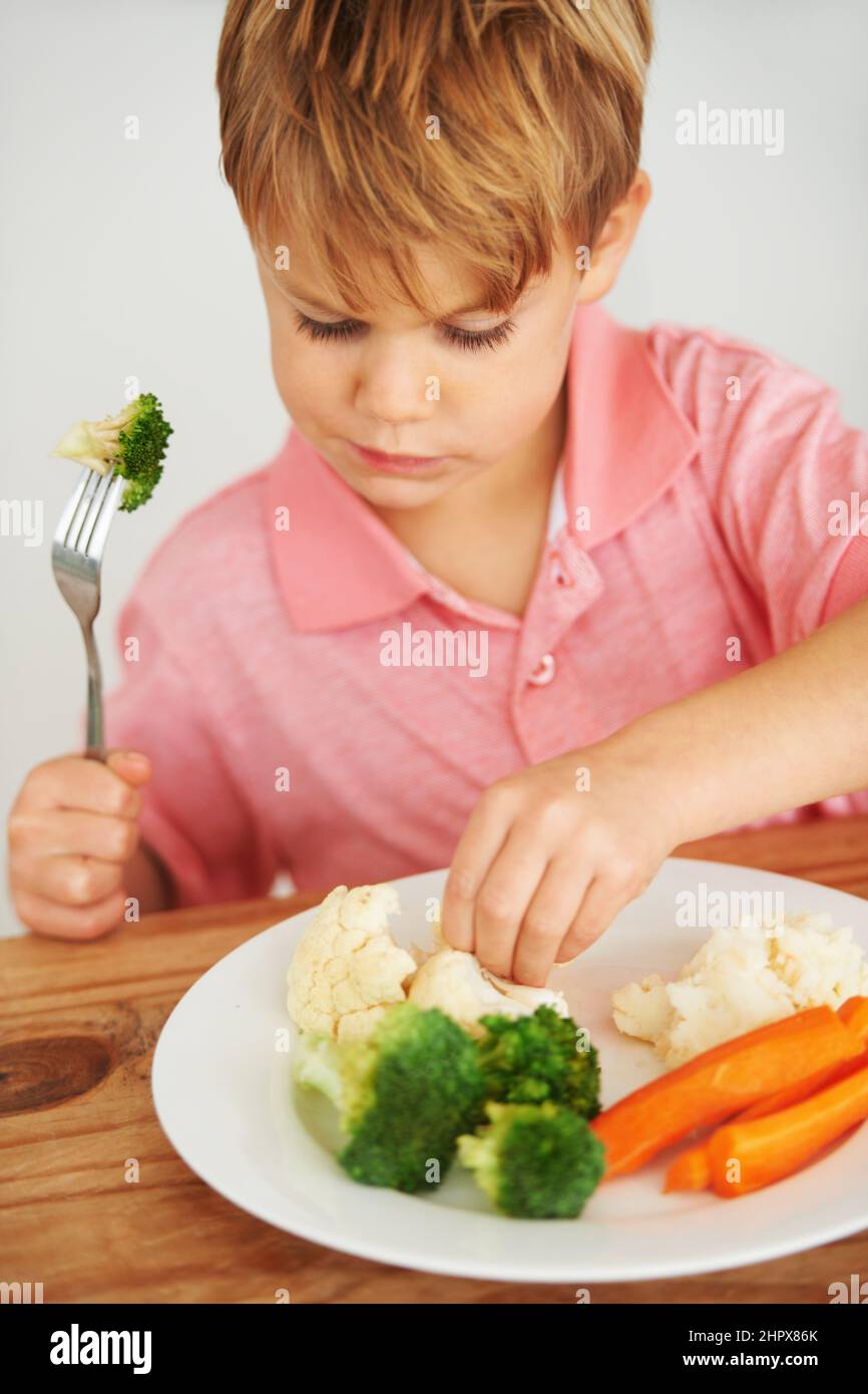 Mom said I have to try these.... A cute young boy playing with the vegetables on his plate. Stock Photo