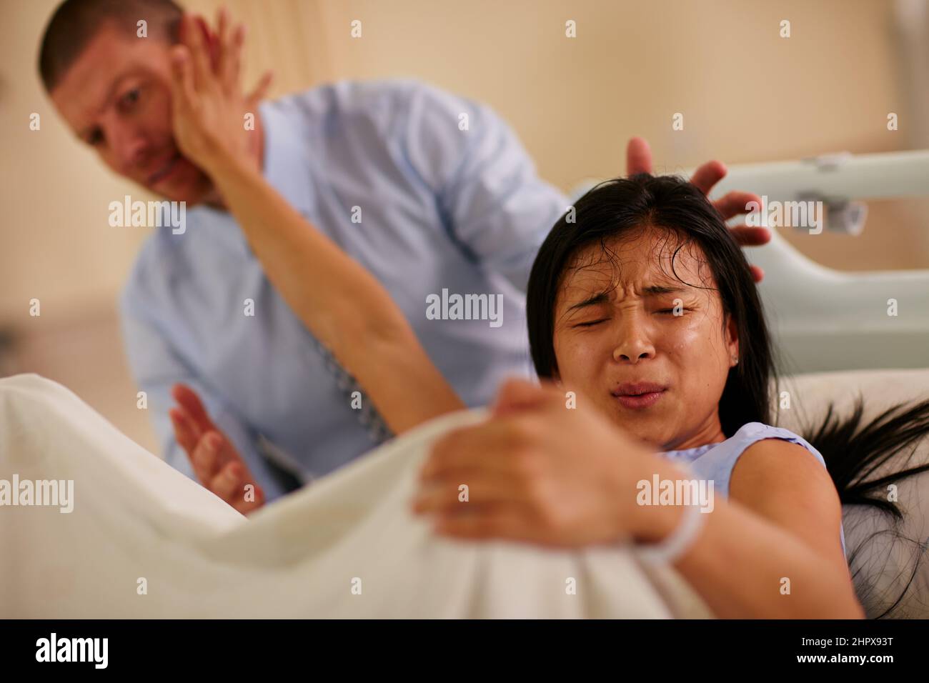 Youre not helping.... Shot of a young woman giving birth with her husband supporting her in the background. Stock Photo