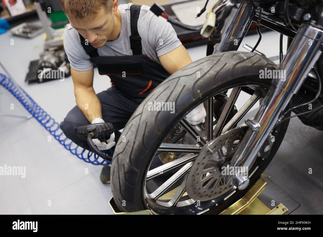 In garage, a repairman in overalls sits near wheel motorcycle Stock Photo