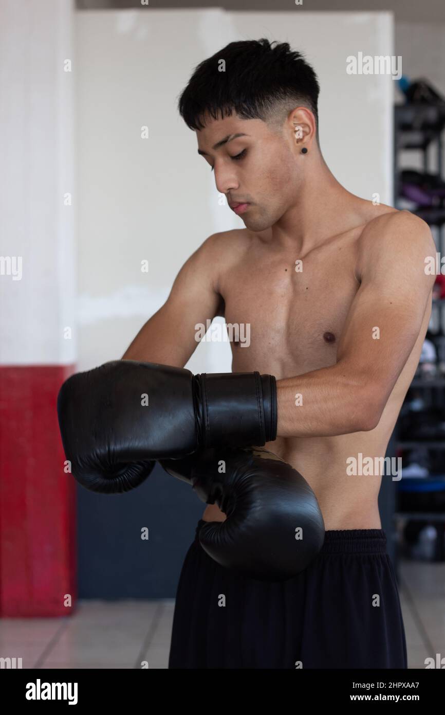 young mexican boxer with gloves on hitting the bag during his training inside the gymnasium Stock Photo