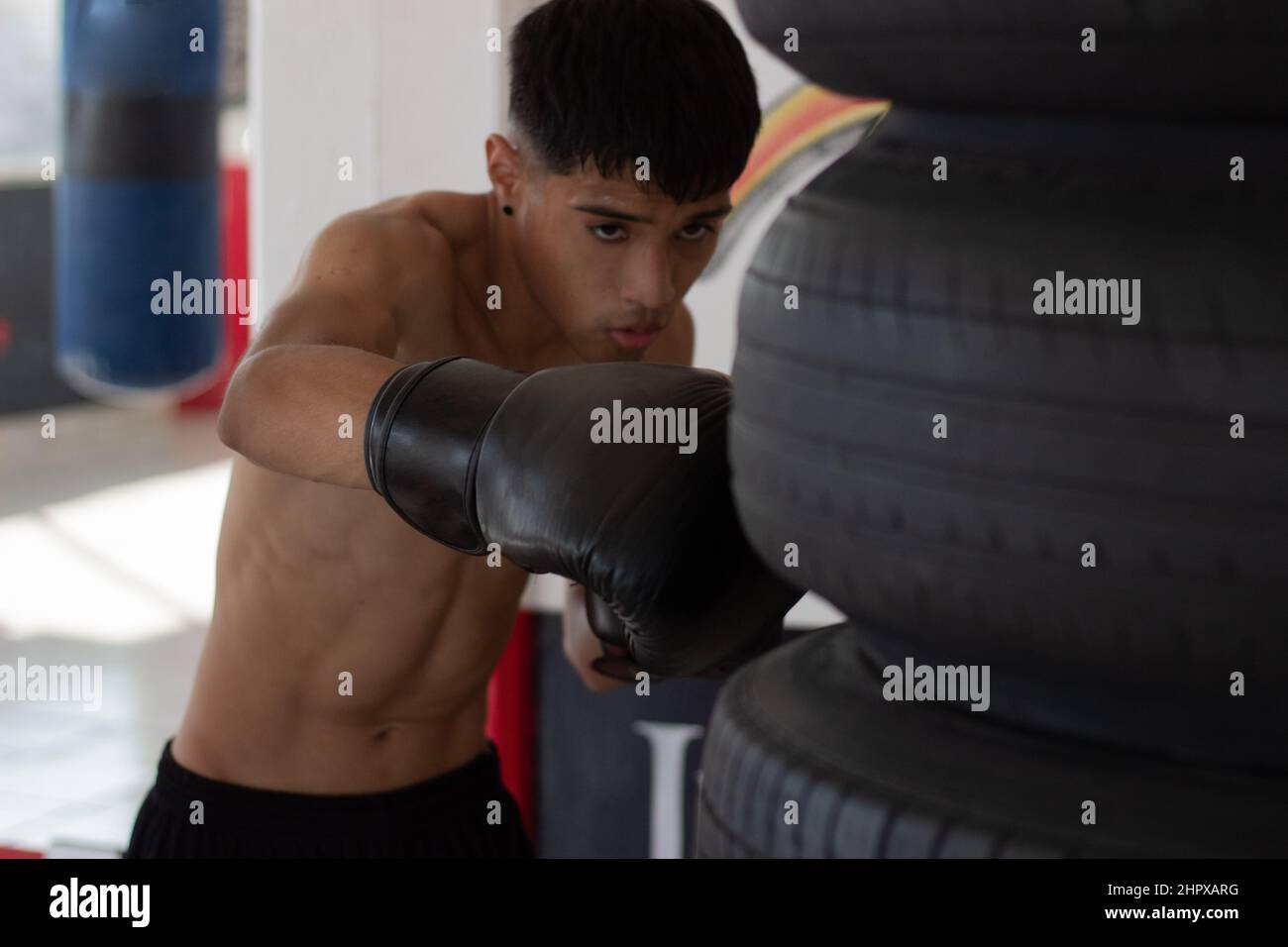 young mexican boxer with gloves on hitting the bag during his training