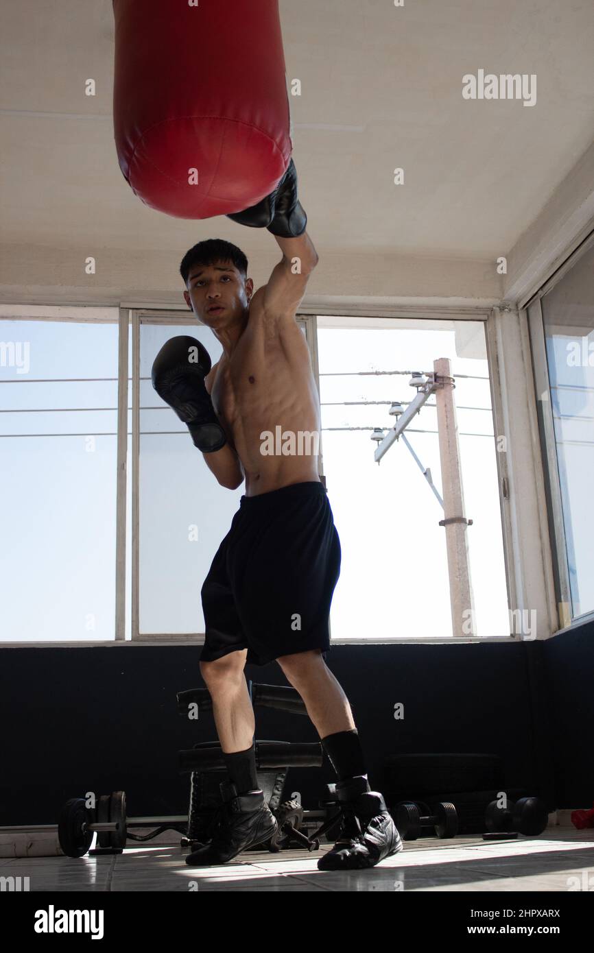 young mexican boxer with gloves on hitting the bag during his training