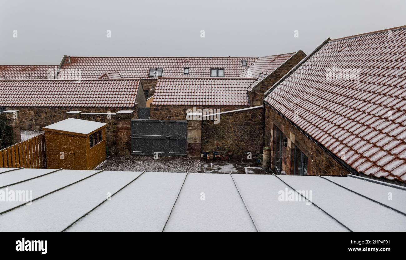 East Lothian, Scotland, UK, 24th February 2022. UK Weather: Snow falling over rooftops of converted steading houses in Winter Stock Photo
