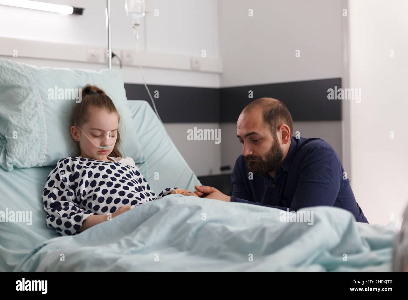 Sick young girl sleeping in hospital bed while worried father sitting ...