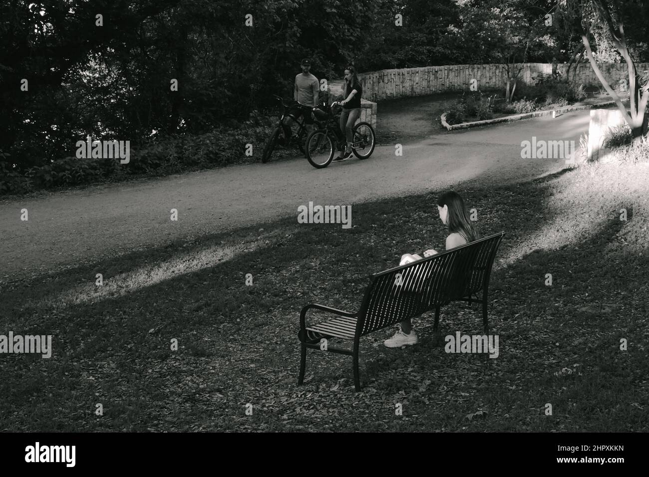 Girl sitting on a park bench reading a book Stock Photo - Alamy