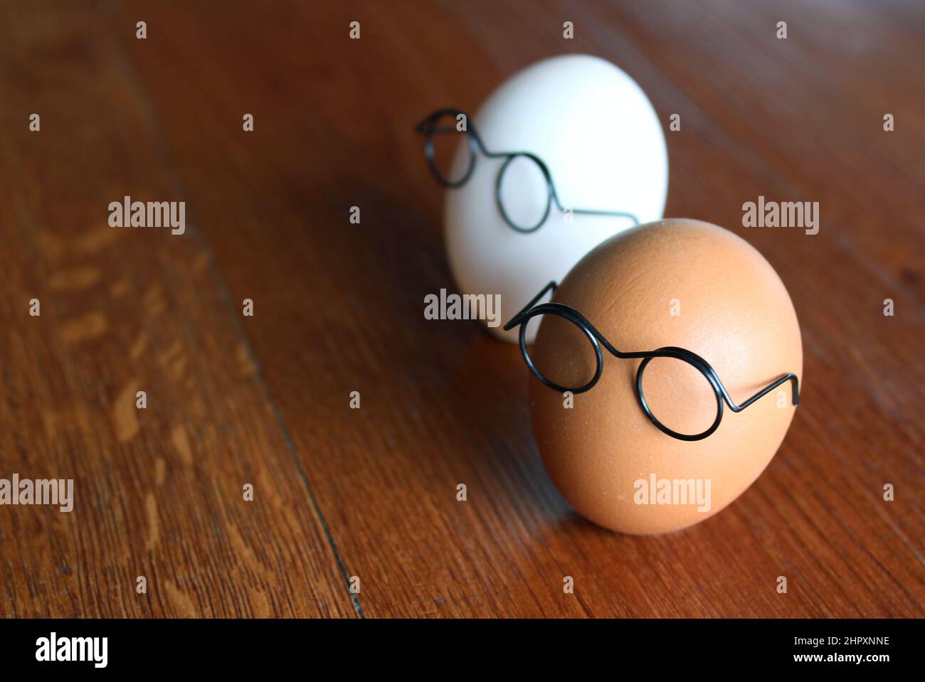 Similar but different concept. White egg and brown egg wear glasses on wooden table Stock Photo