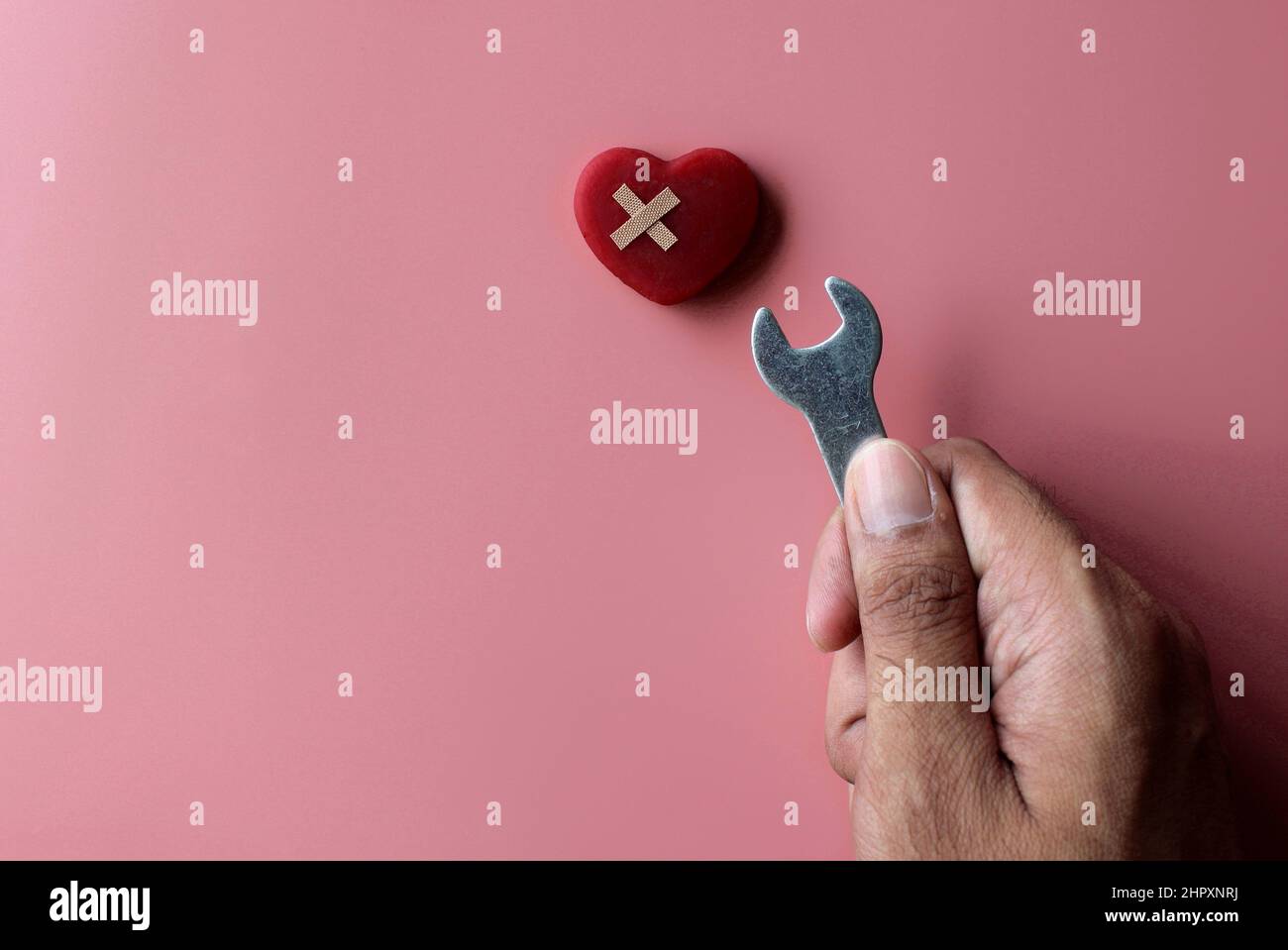 Fix, mend a broken heart concept. Red heart, bandage and spanner on pink background with copy space. Stock Photo