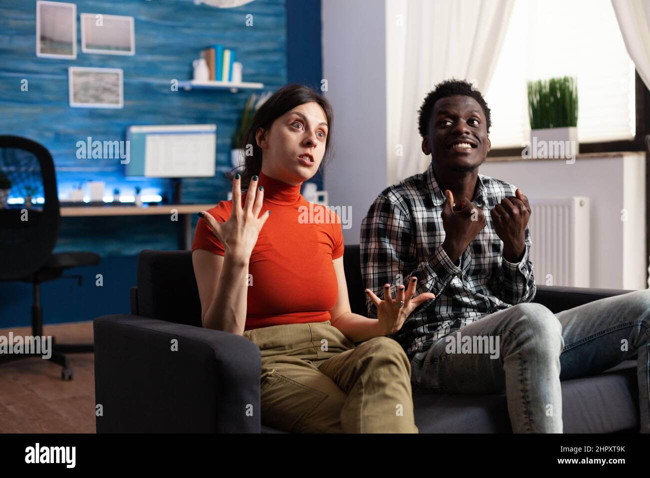 Angry multiracial persons reacting goofy over unhealthy conflict while gesturing agressively. Irritated adults fight over marriage problems while at home in living room on couch Stock Photo