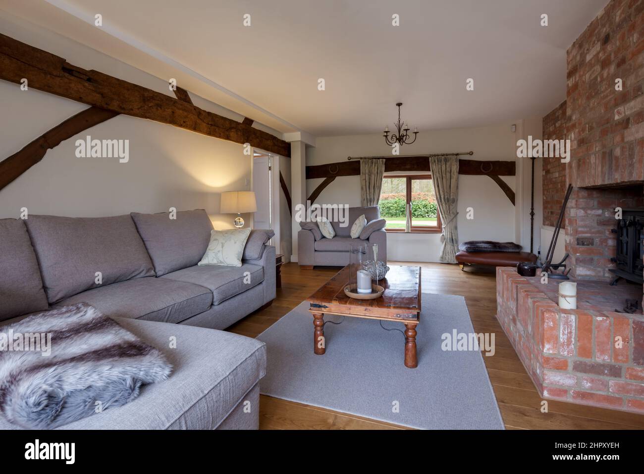 Modern looking furnished sitting room lounge within renovated old property with exposed brick fireplace and hearth, brightly decorated in shades of wh Stock Photo