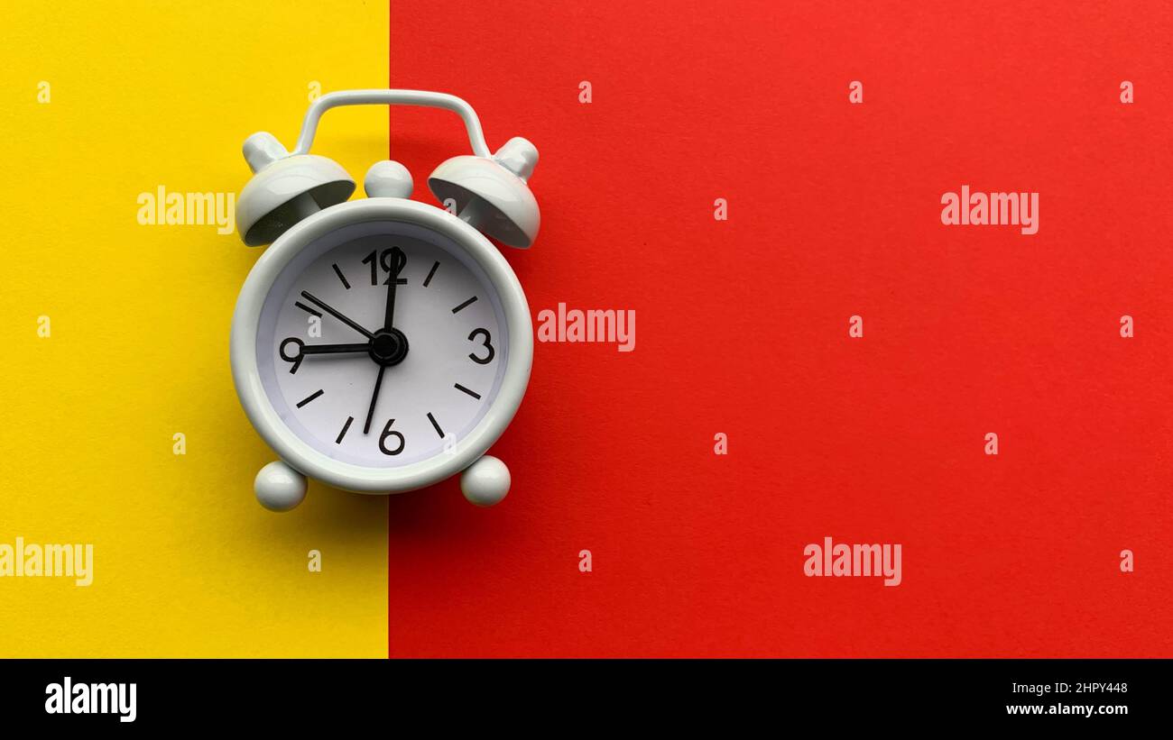 White alarm clock on with yellow and red background. Conceptual Stock