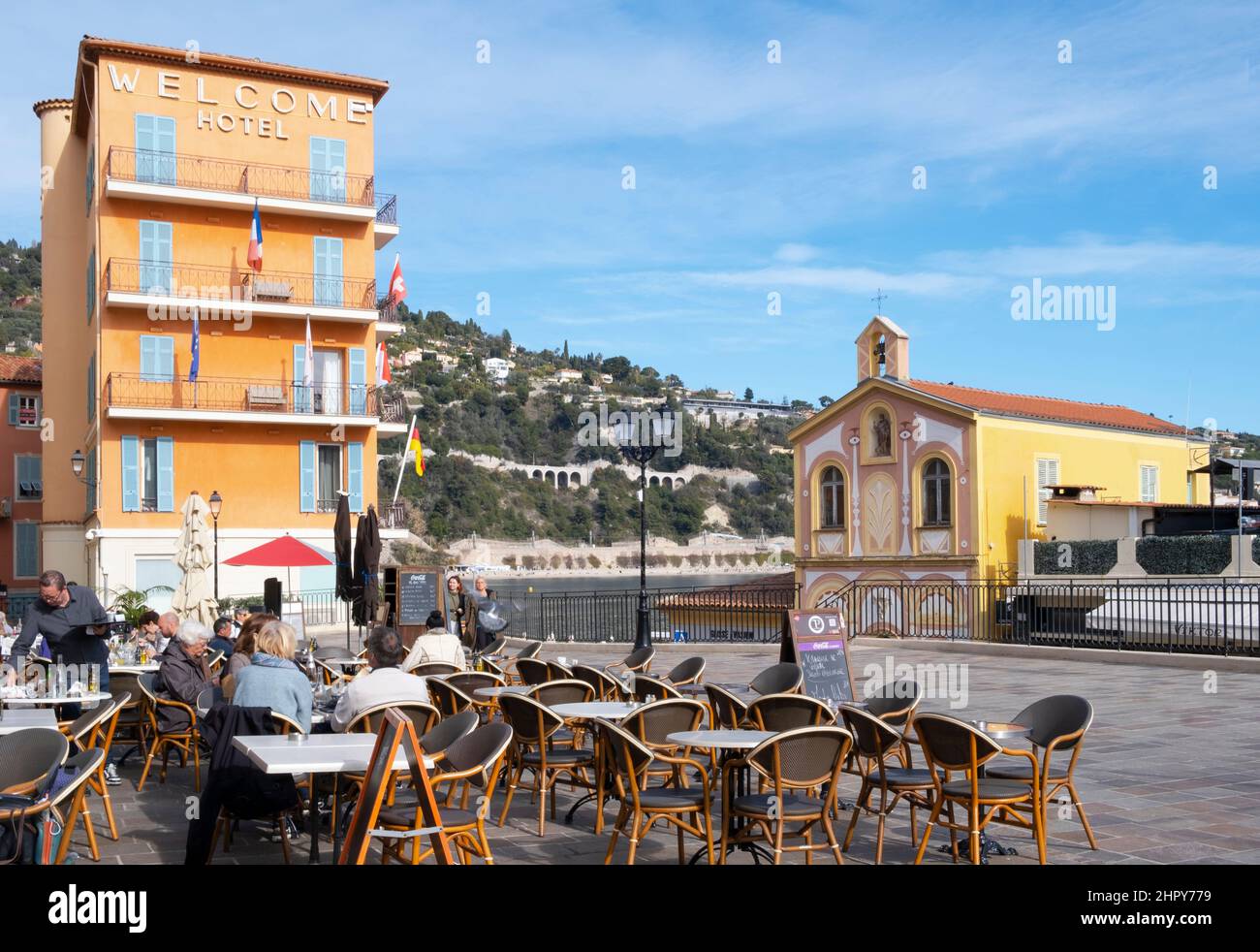 Visitors at a terrace cafe next to the Chapelle St Pierre des Pecheurs overlooking the harbour in Villefranche sur Mer, Cote d'Azur, France Stock Photo
