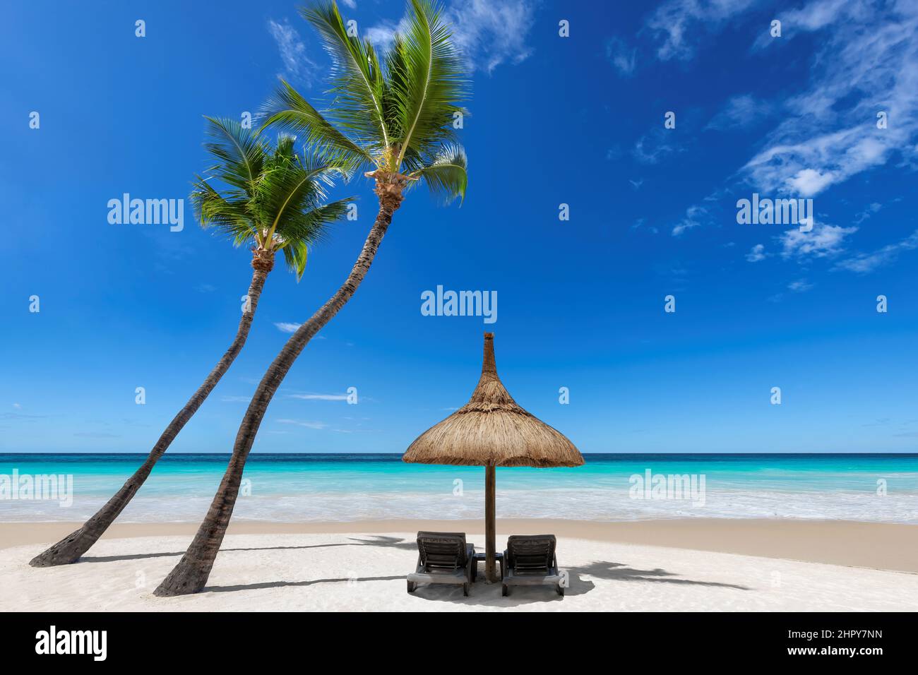 Beach umbrella and chairs on sandy beach with coco palms and turquoise sea. Stock Photo