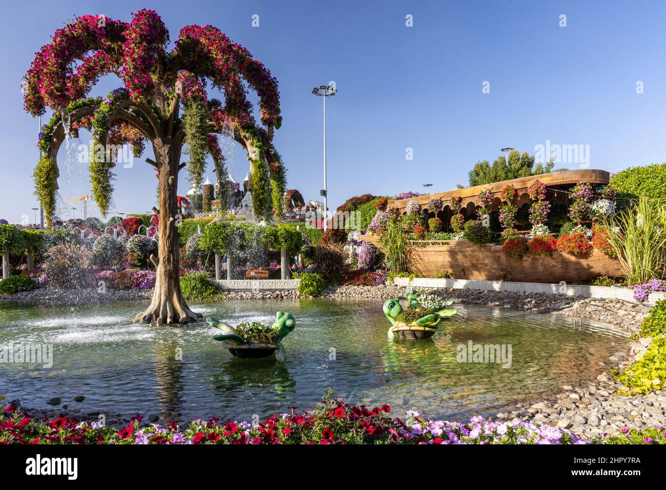 A pond at the Dubai Miracle Garden with a palm tree-shaped fountain and sculptures of turtles-flower pots. Stock Photo