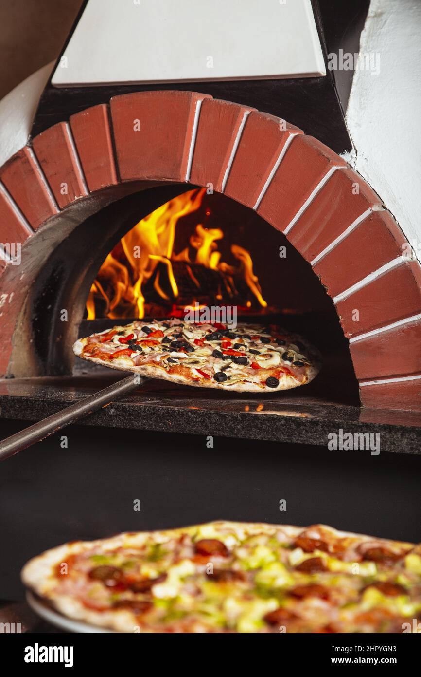 Vertical shot of traditional Italian pizza cooking in a wood stone oven Stock Photo