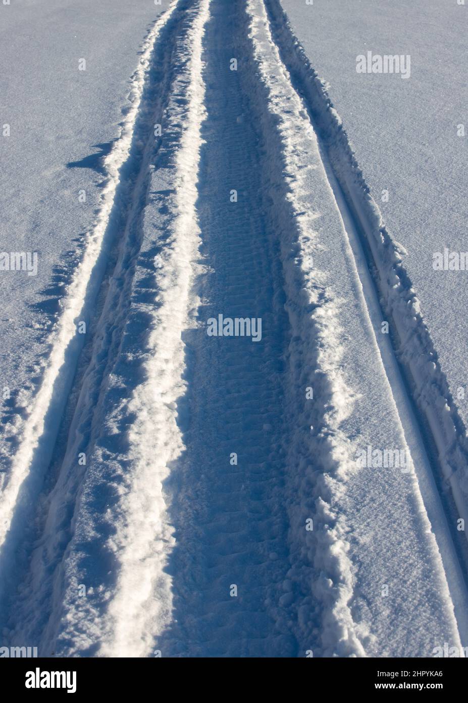 Vertical shot of snowmobile tracks on the snow under the sunlight Stock