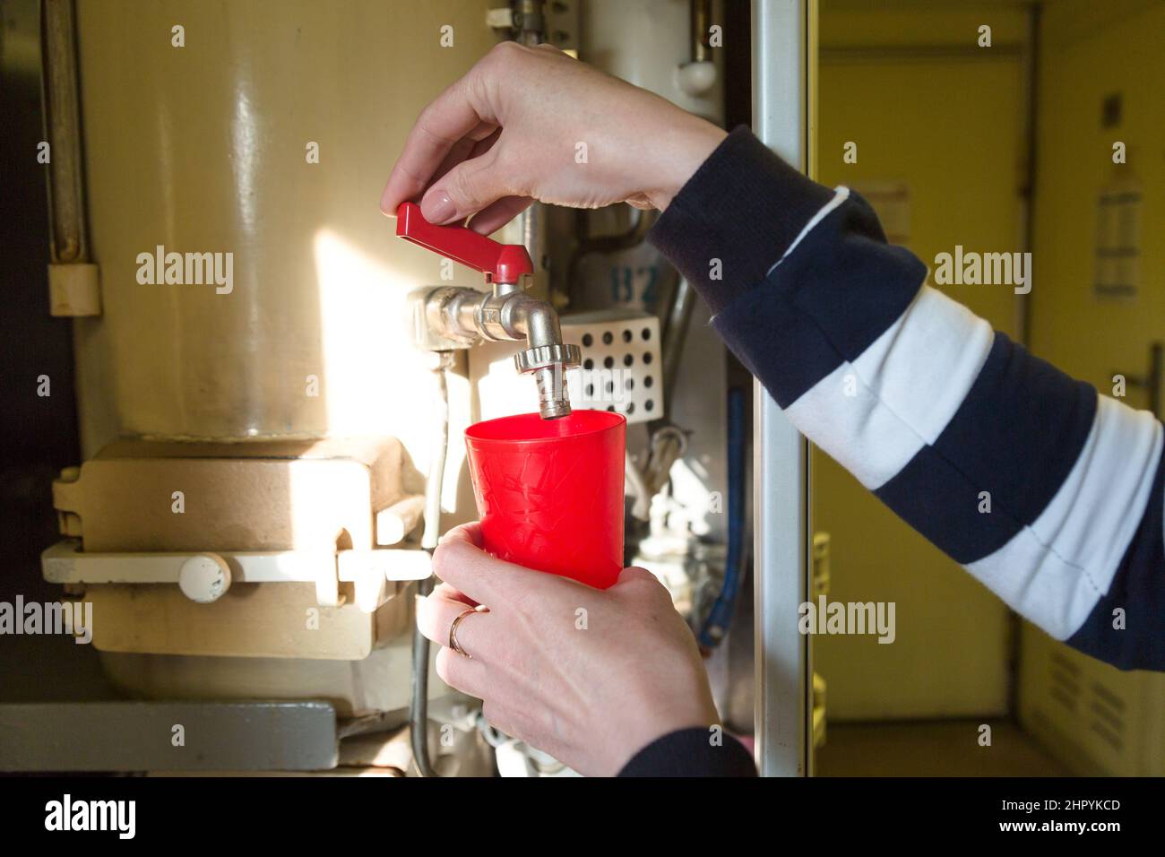 A woman's hand pouring boiling water into a red glass in a train car