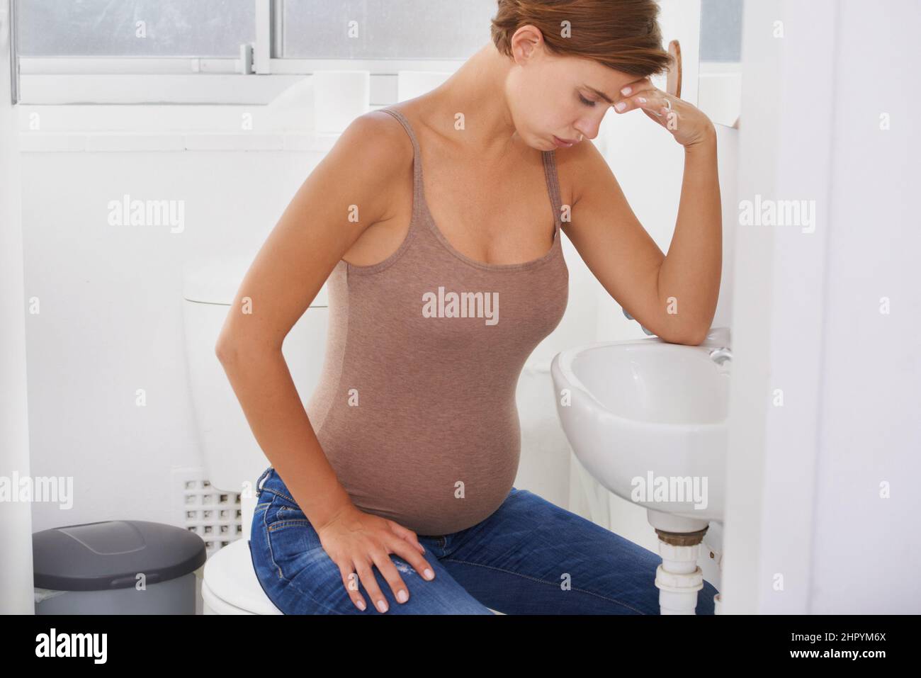 Riding waves of nausea. A pregnant woman struggling with morning sickness in the bathroom. Stock Photo