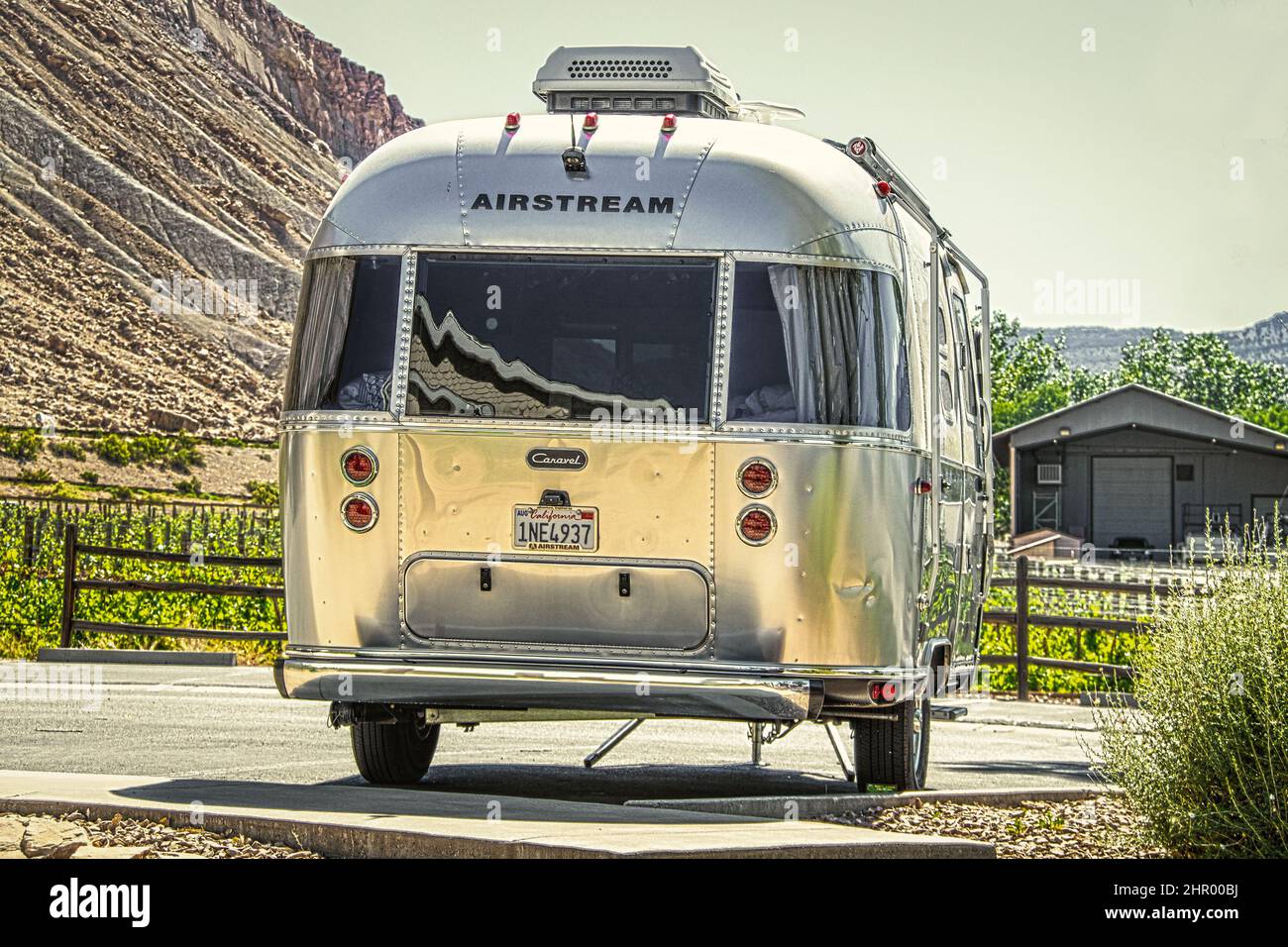 2021 06 04 Grand Junction Colorado USA - Airstream camper trailer parked on concrete with grape vineyards and mesa and barn behind it. Stock Photo