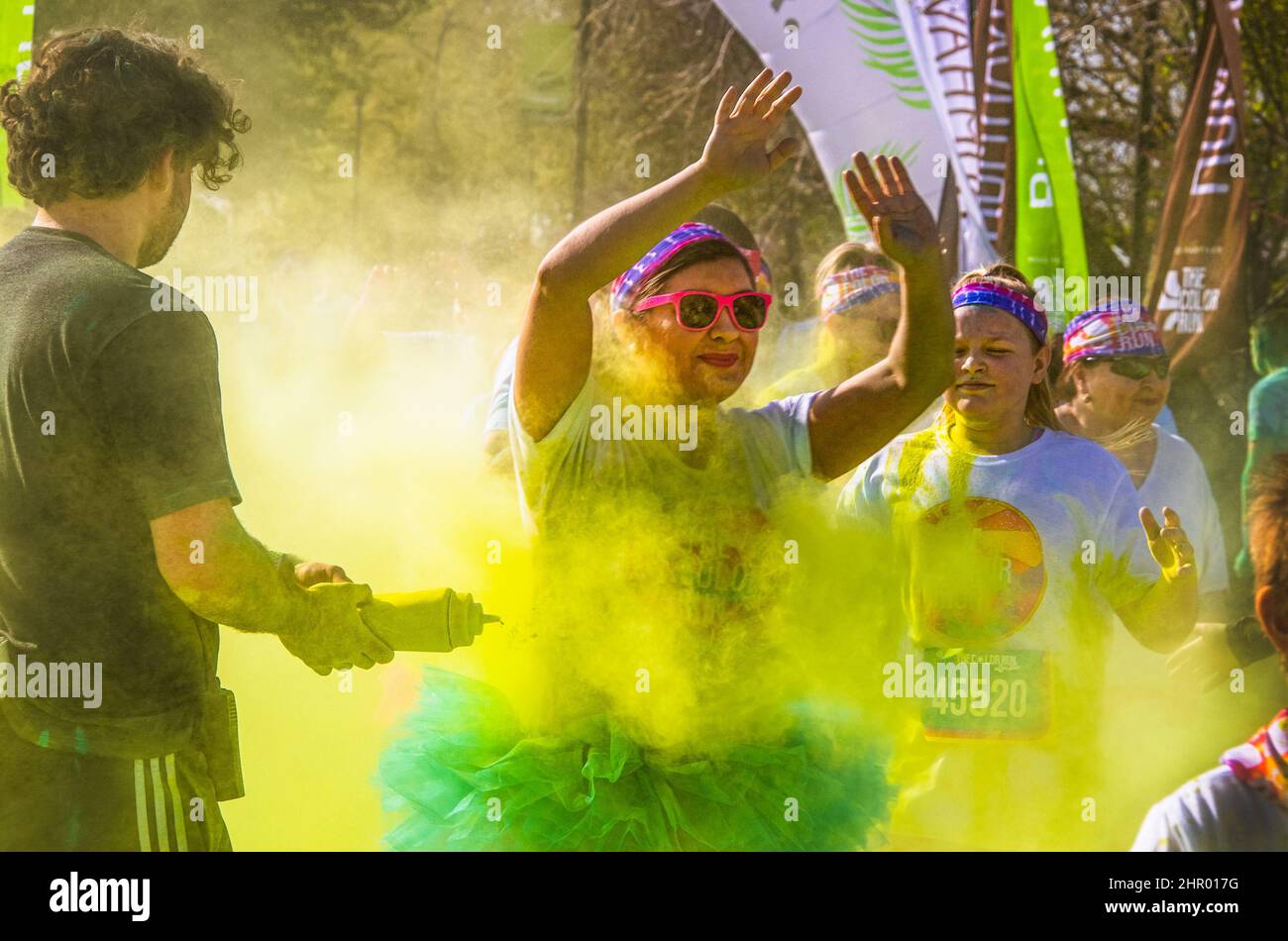 April 6 2019 Tulsa USA - Holi - Color Run in Tulsa USA - Girls in ballerina skirts raise hands over head as curly haired volunteer squirts them with y Stock Photo