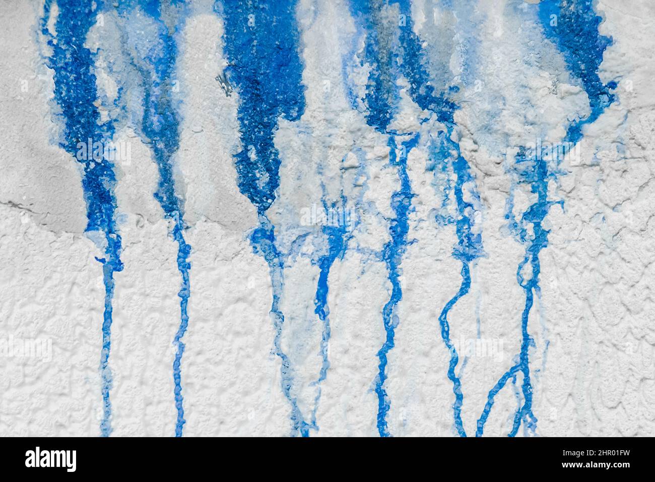 Streaks of liquid spilled blue paint down the white plaster wall