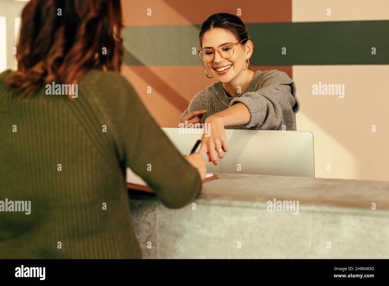 Easygoing receptionist assisting a woman with signing in to an office. Friendly receptionist showing a woman where to sign on a clipboard. Young woman Stock Photo