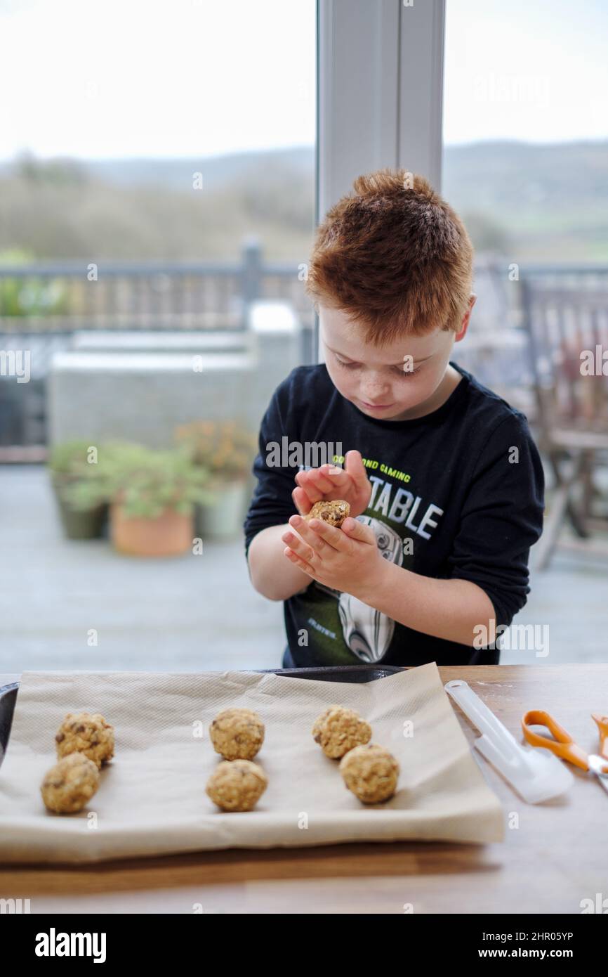 A young boy rolls a cake mixture, using his hands, into a ball shape. The rolls of mixture is then placed onto a baking tray for baking into cookies Stock Photo