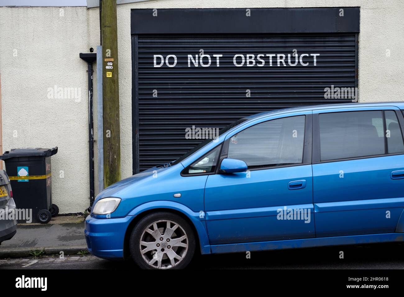 A car parked on a uk residential street obstructing a garage that is clearly displaying a large do not obstruct request across its door. Stock Photo