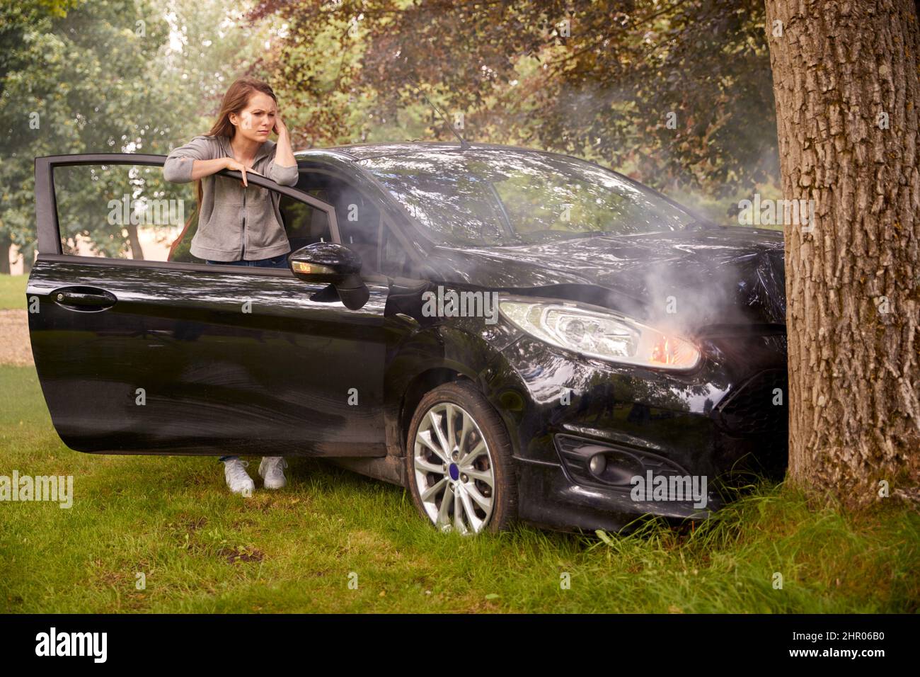 Woman Next To Car Crashed Into Tree Inspecting Accident Damage Stock Photo