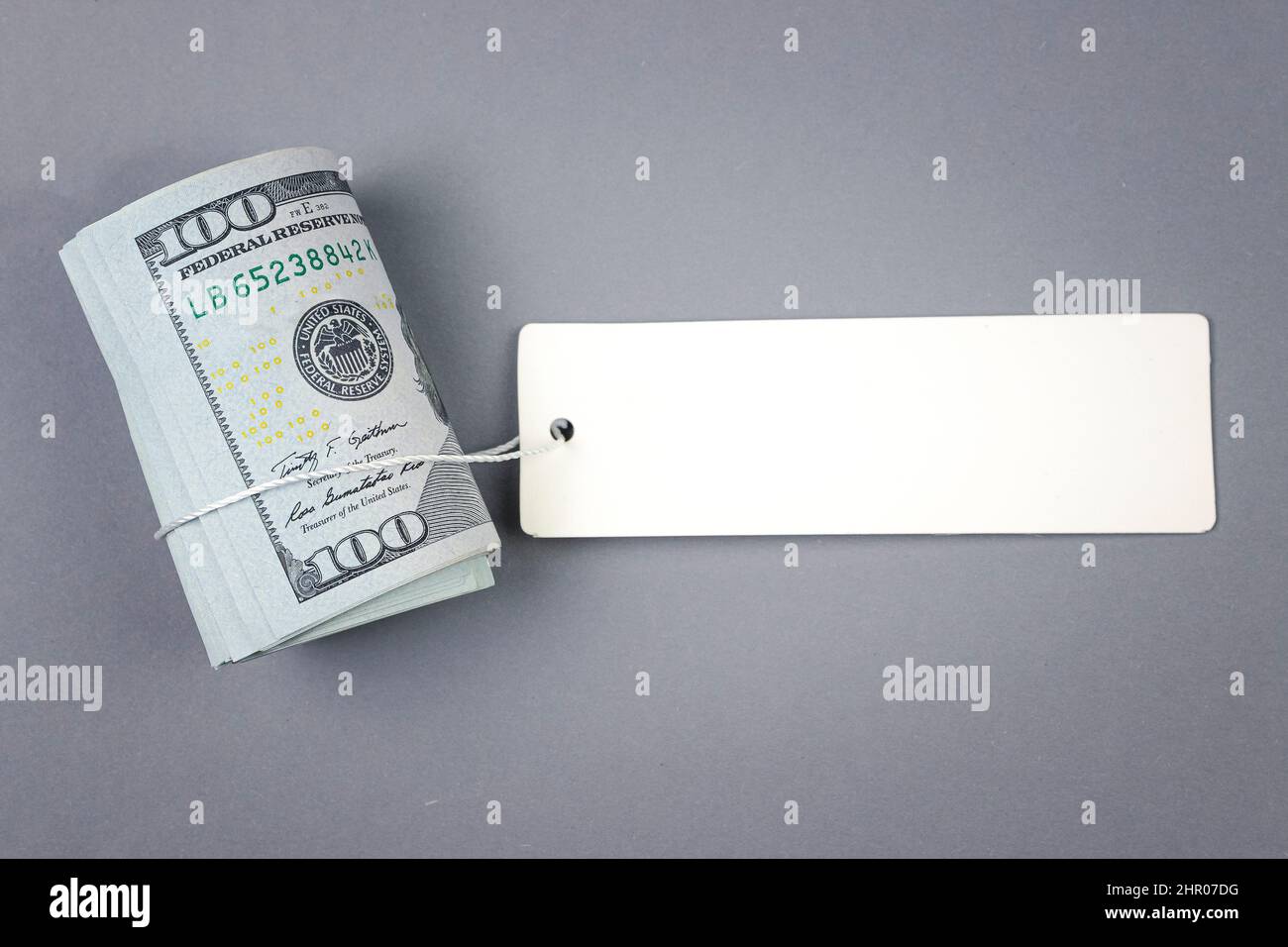 Roll of money with blank white cardboard price tag or label. One hundred American dollars, viewed from above with copy space Stock Photo
