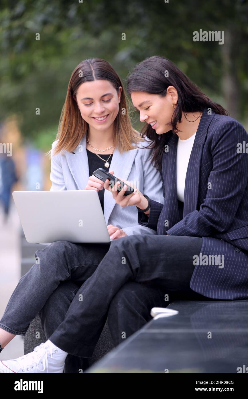 Female Office Workers Outdoors Working On Laptop And Using Mobile Phone During Break From The Office Stock Photo