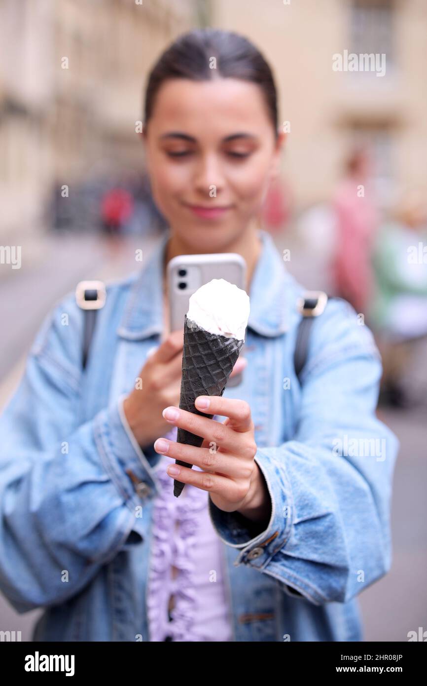 Young Woman Taking Photo Of Ice Cream Cone With Mobile Phone To Post On Social Media Stock Photo