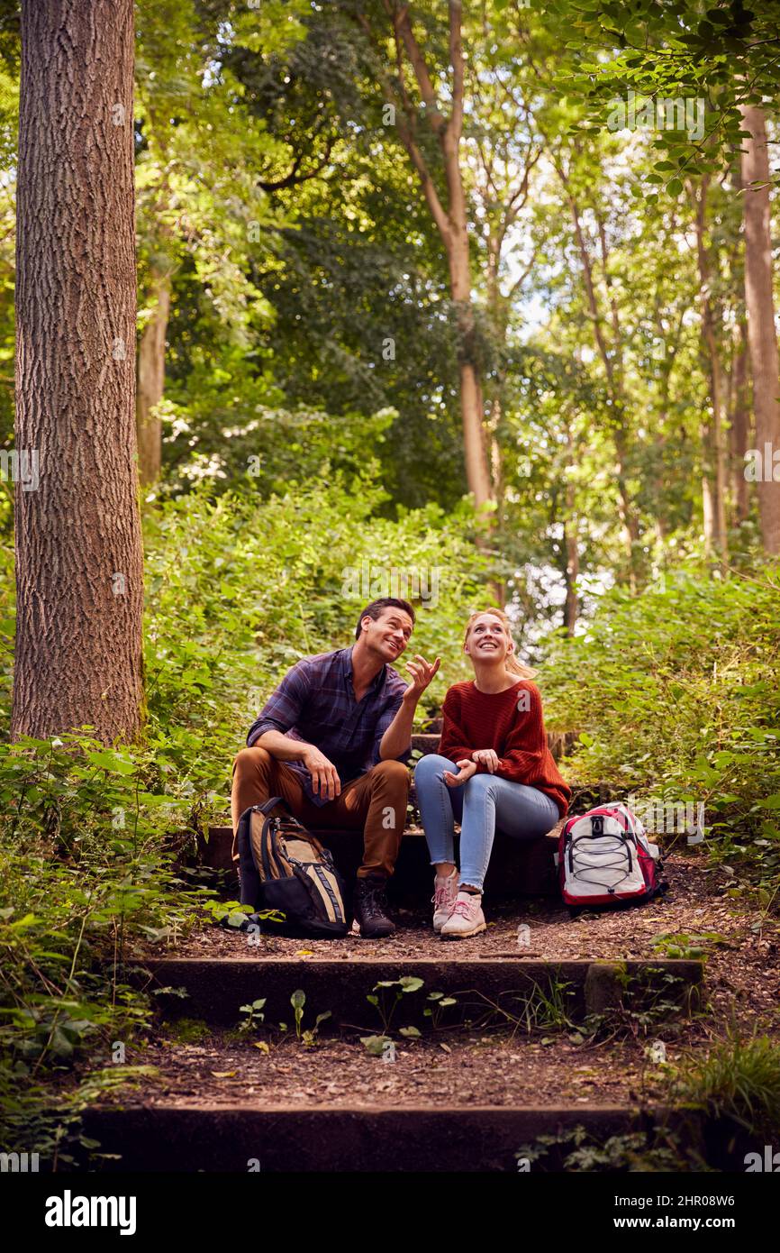 Couple In Countryside Hiking Along Path Through Forest Sit And Take A Break Together Stock Photo