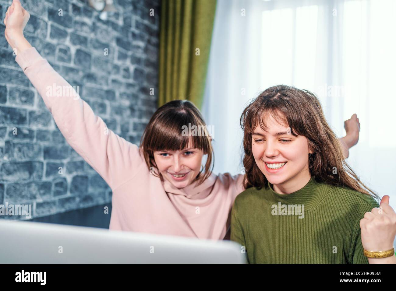 Young caucasian girls receive good news or winning lottery looking at laptop. Happy surprised girl gets positive emotion. Stock Photo