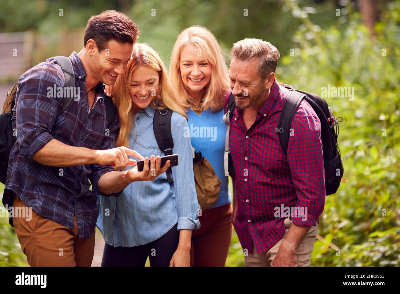 Group Of Friends Hiking In Countryside Looking At Picture On Phone As They Hike Along Path Stock Photo