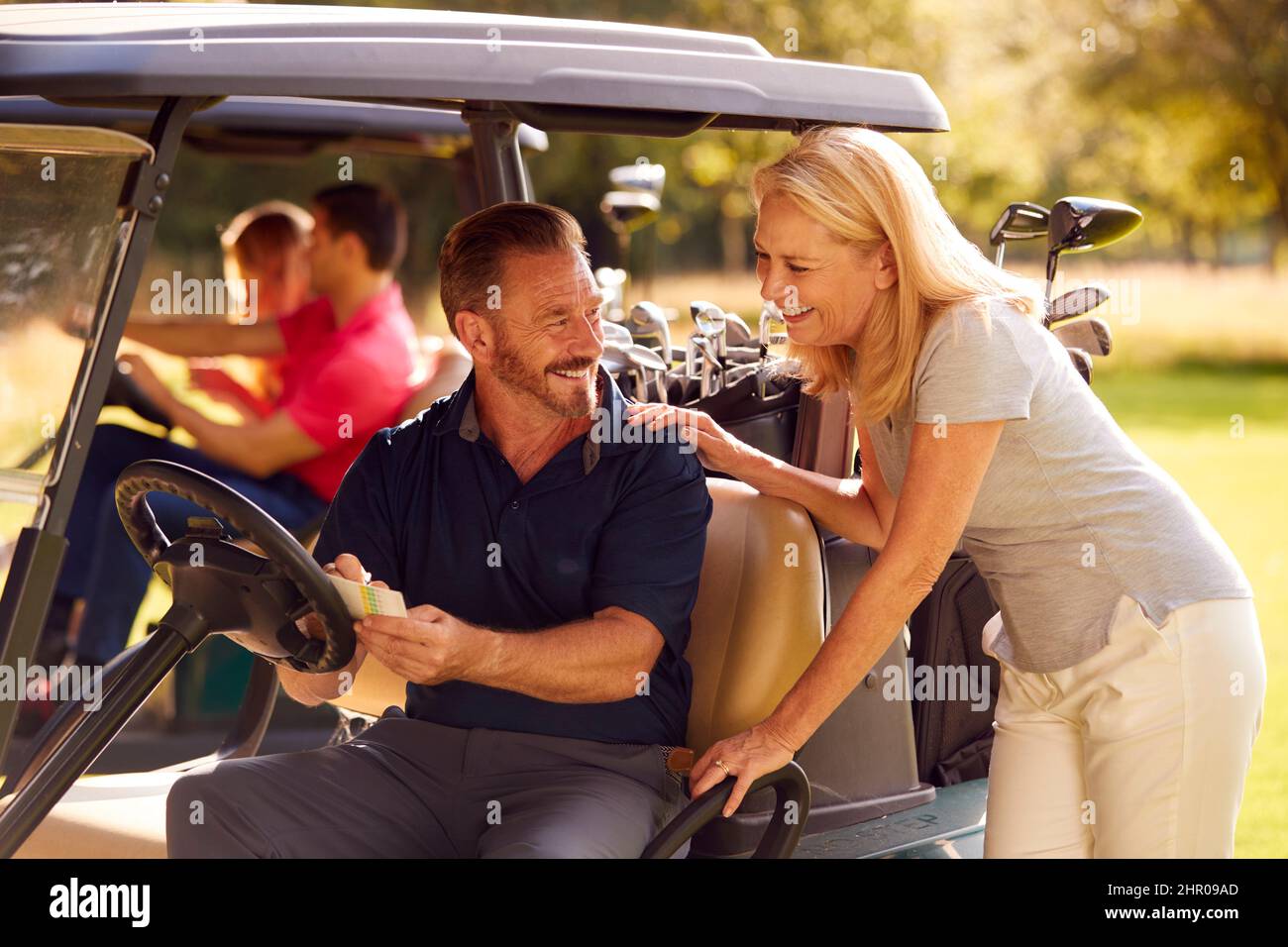 Mature And Mid Adult Couples In Buggies Playing Round On Golf Together Stock Photo