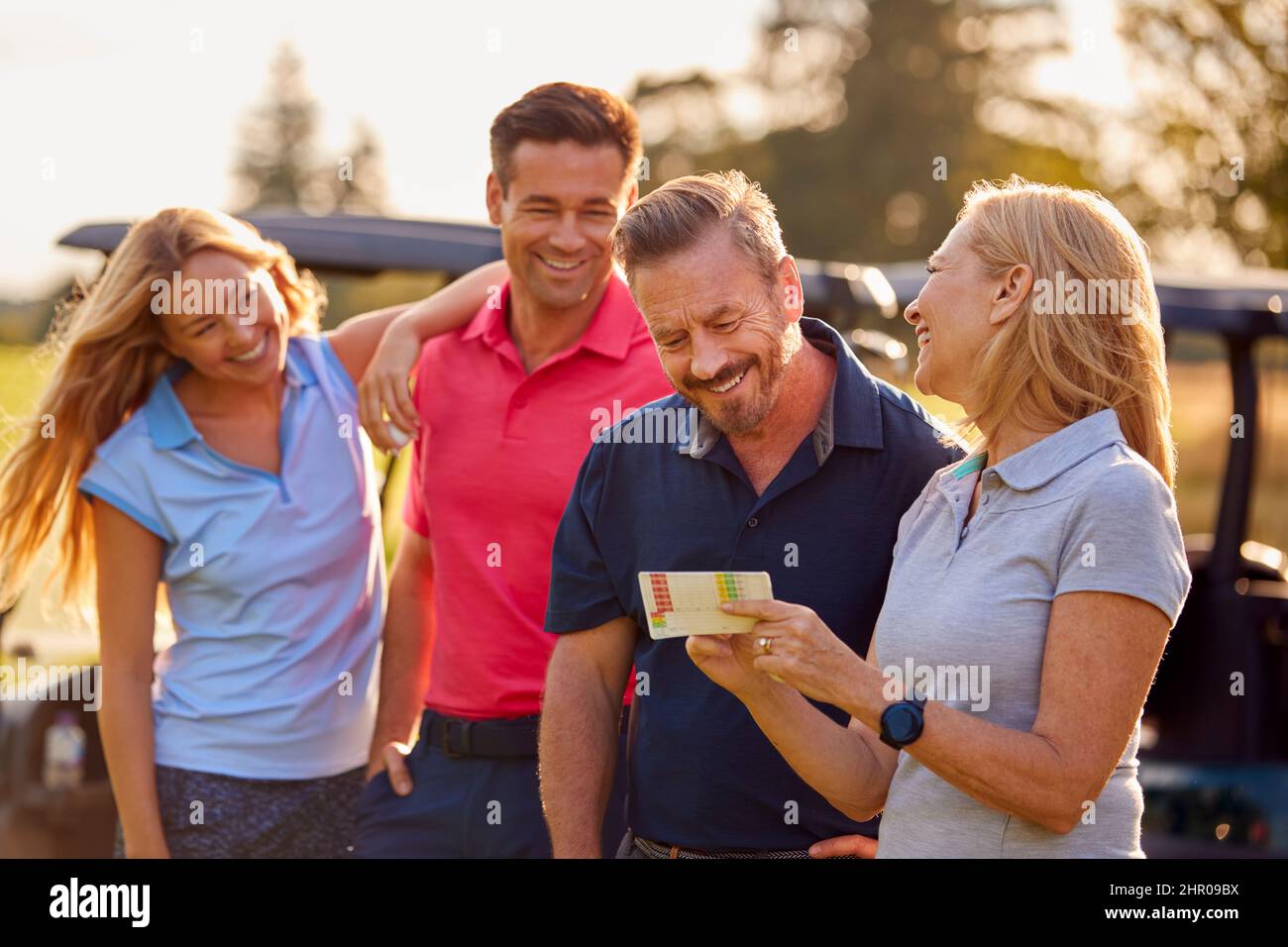 Mature And Mid Adult Couples Standing By Golf Buggy Checking Score Cards Together Stock Photo