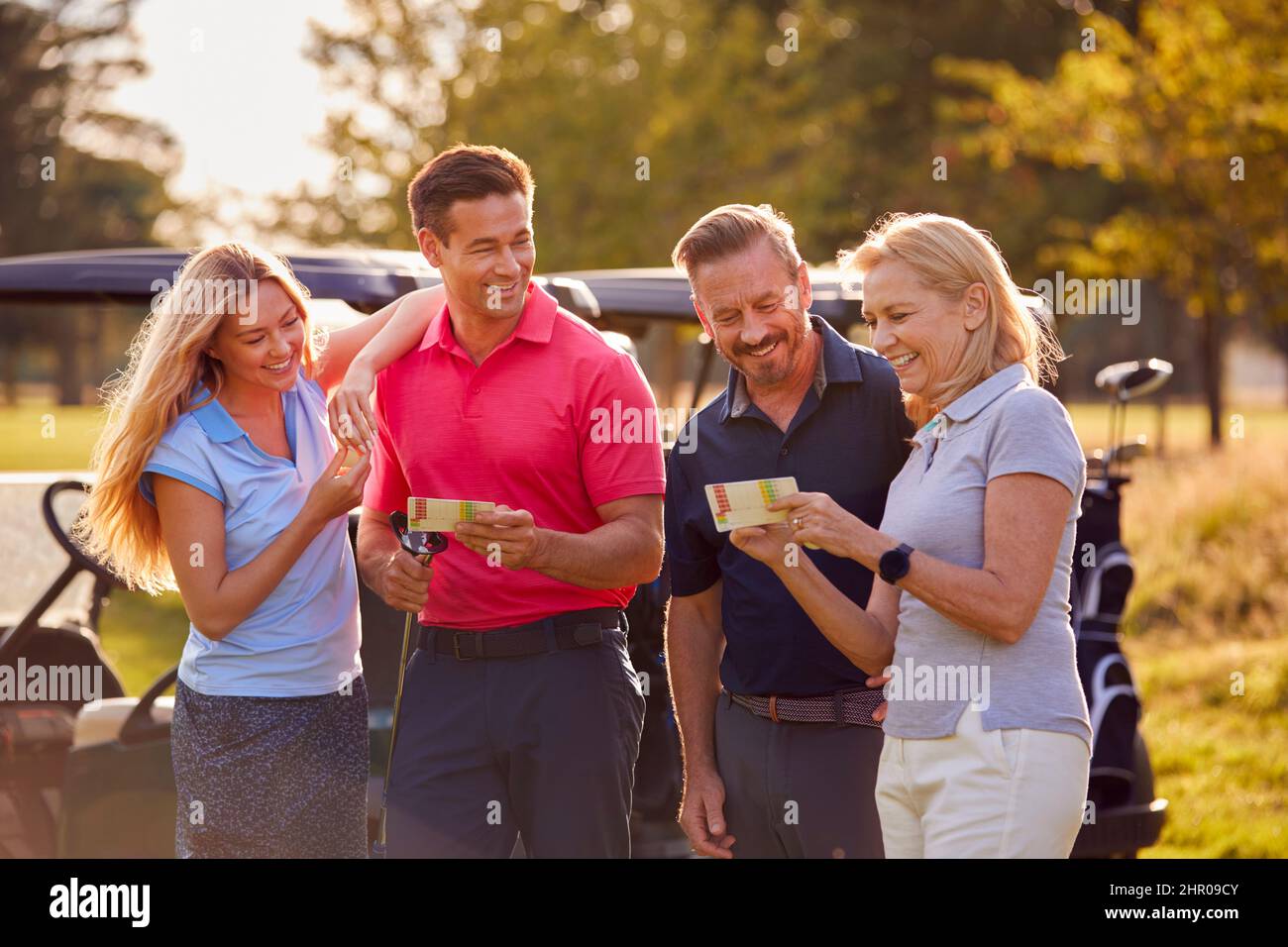 Mature And Mid Adult Couples Standing By Golf Buggy Checking Score Cards Together Stock Photo