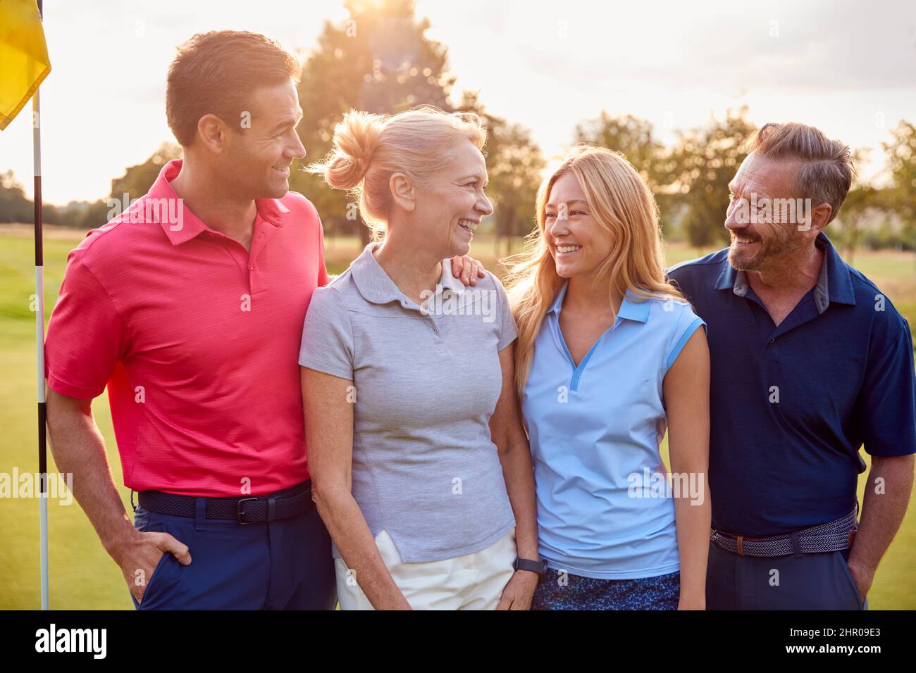 Mature And Mid Adult Couples Standing By Flag On Green Playing Round Of Golf Together Stock Photo