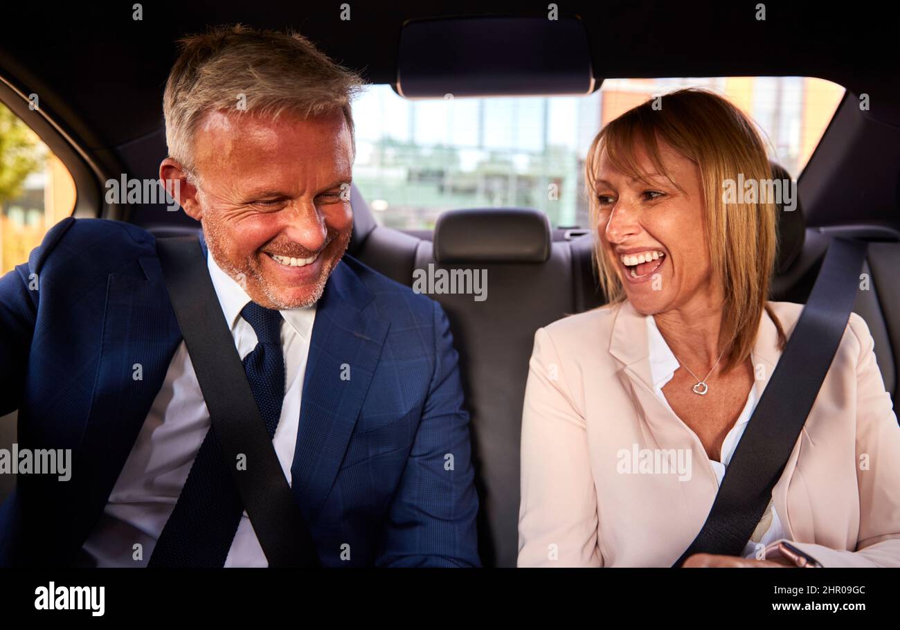 Smiling Businessman And Businesswoman In Back Of Taxi Driving To Office Meeting Together Stock Photo