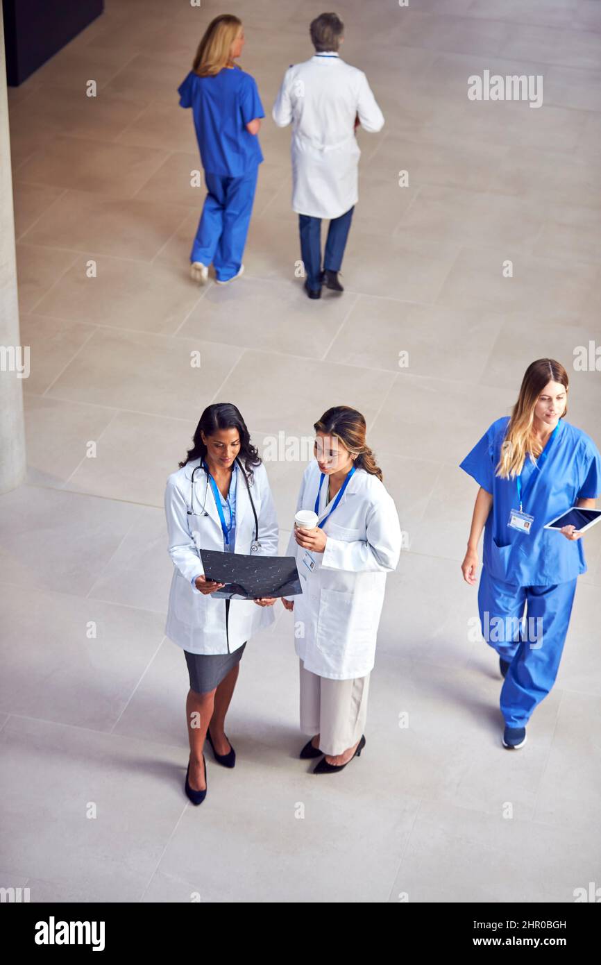 Overhead Shot Of Two Female Medical Staff In White Coats Discussing Patient Scan In Busy Hospital Stock Photo