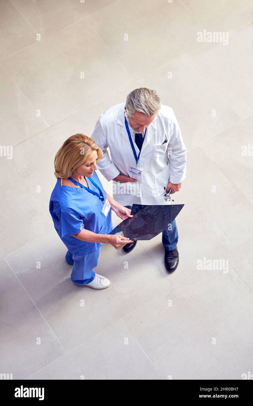 Overhead Shot Of Male Doctor Wearing White Coat Discussing Scan With Female Colleague In Scrubs Stock Photo