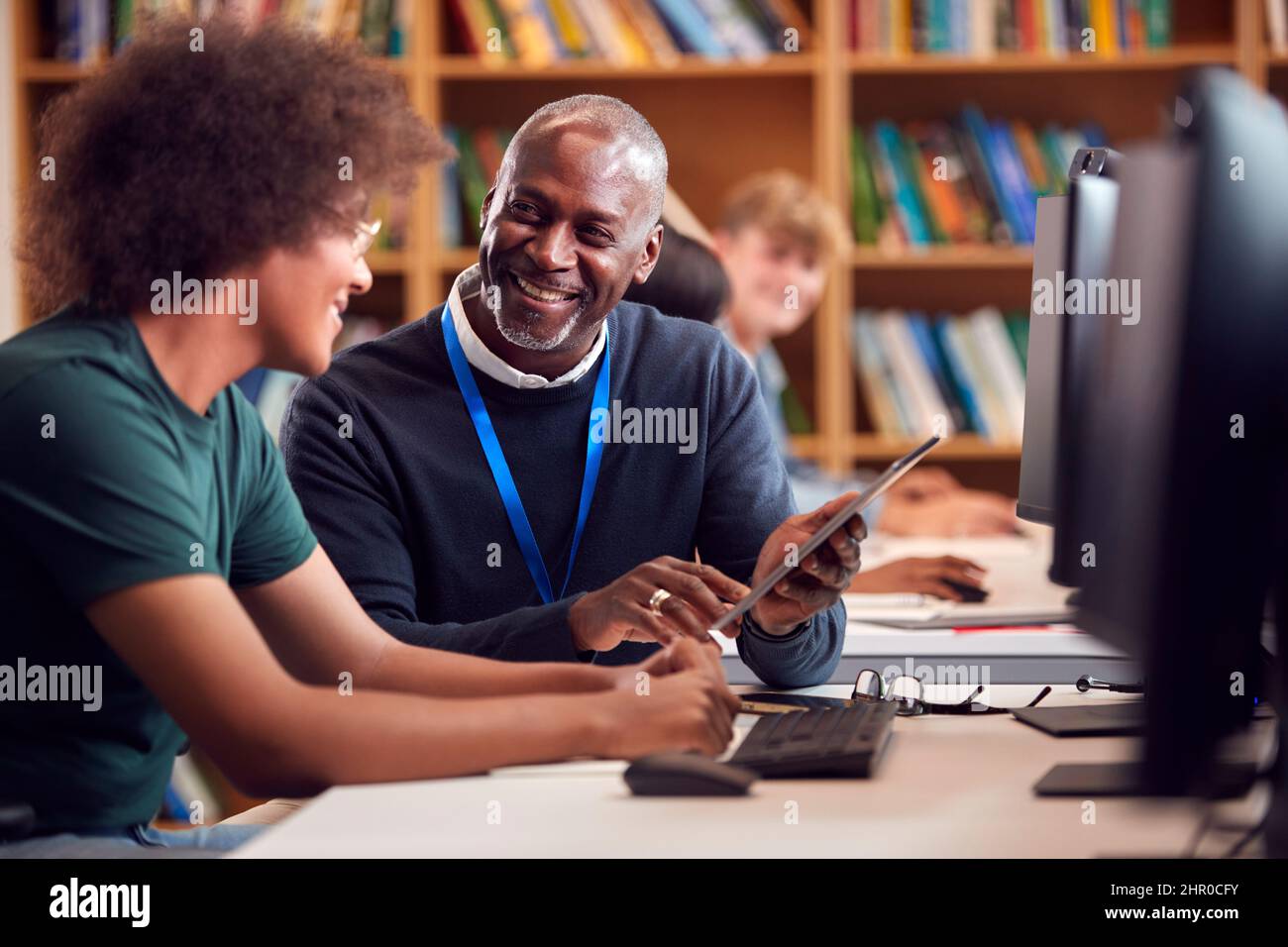 Male University Or College Student Working At Computer In Library Being Helped By Tutor Stock Photo