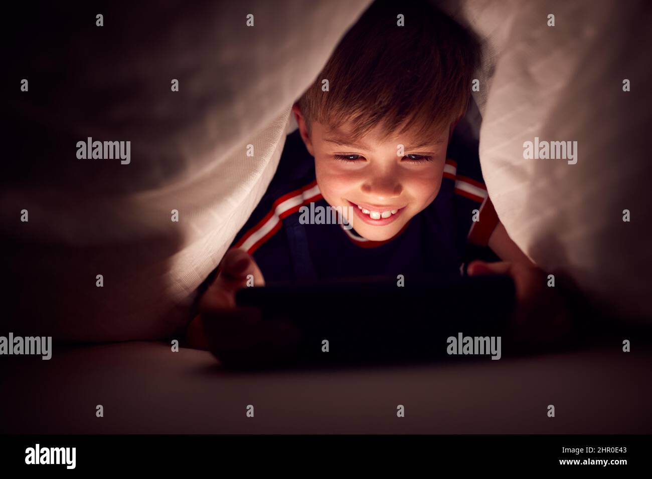 Boy At Home In Bed Under Blankets Watching Movie Or Show On Mobile