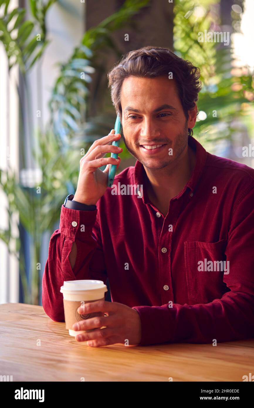 Man Sitting At Table In Coffee Shop Making Call On Mobile Phone Stock Photo