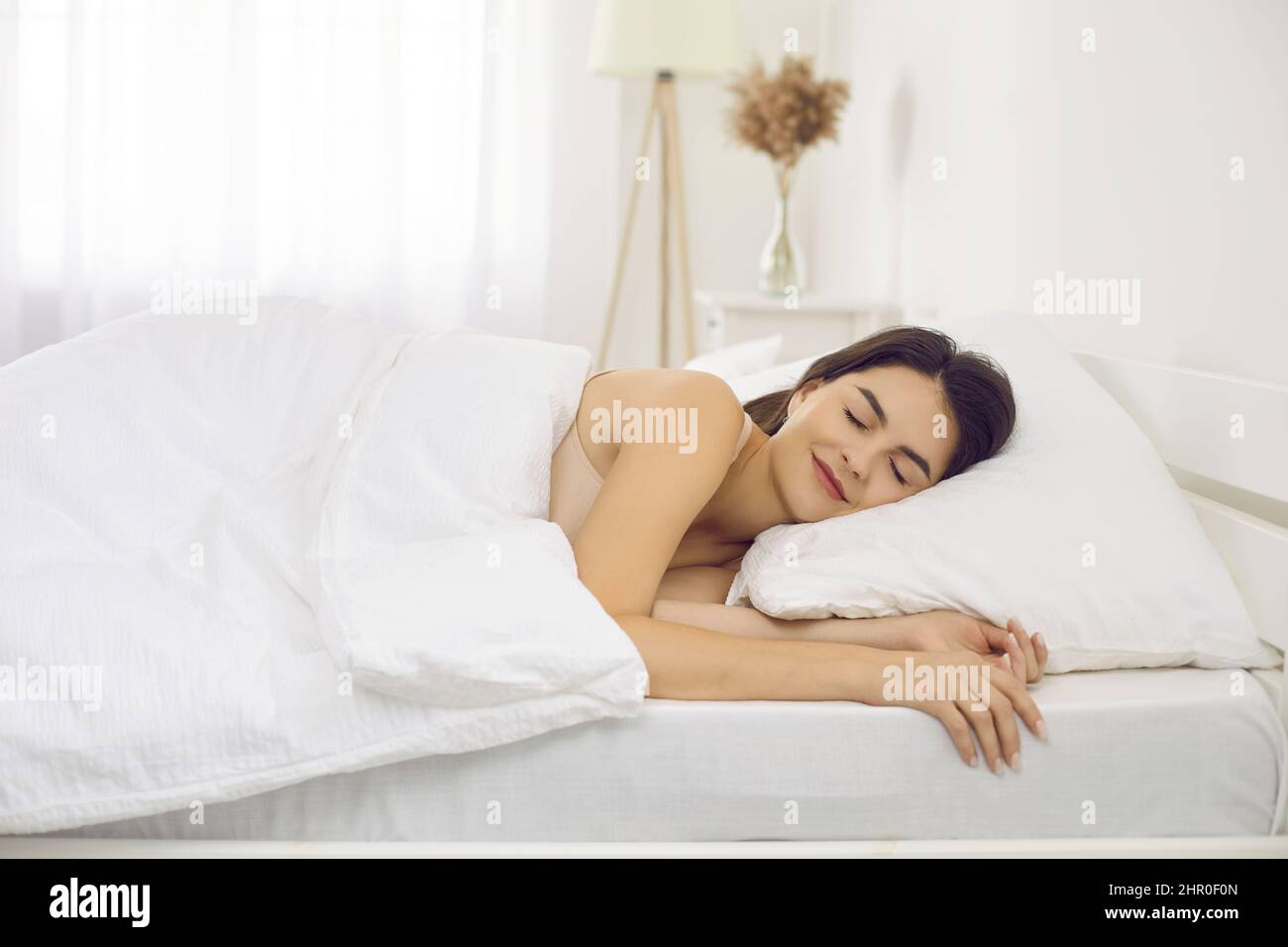 Happy tranquil beautiful woman napping lying on comfortable bedding in bedroom at home alone. Stock Photo