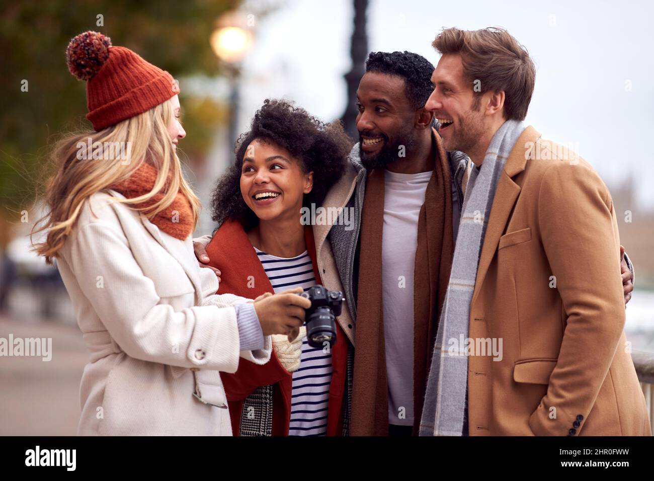 Group Of Friends Outdoors Wearing Coats And Scarves Looking At Photos On Camera In Autumn London Stock Photo