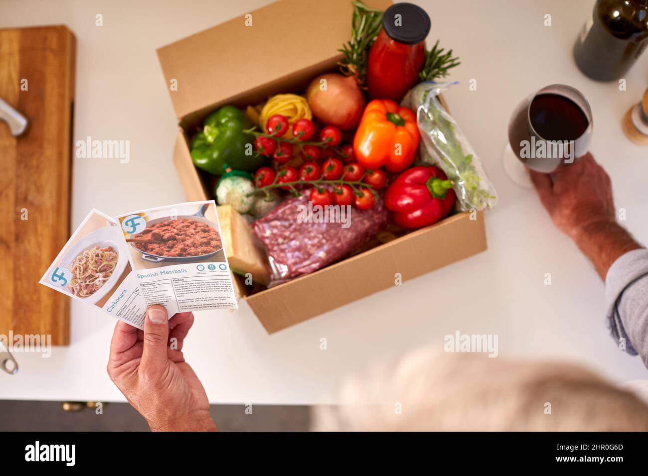 Overhead Of Man In Kitchen Holding Recipe Cards For Online Meal Food Recipe Kit Delivered To Home Stock Photo