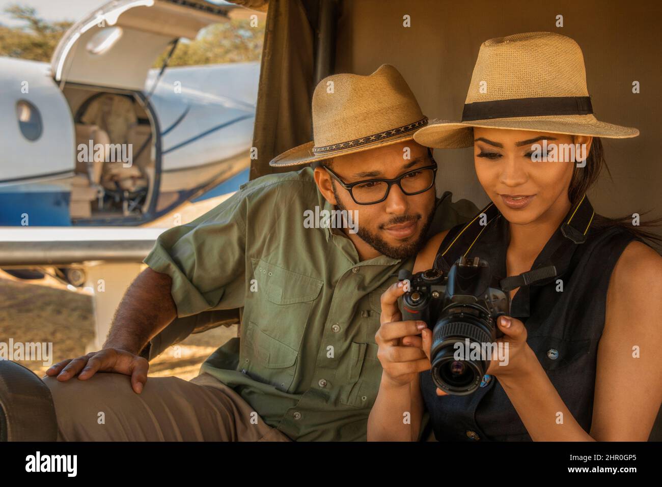 A young, attractive Tanzanian couple wearing tropical clothes, on safari at a game reserve, beside their private chartered aircraft. Stock Photo