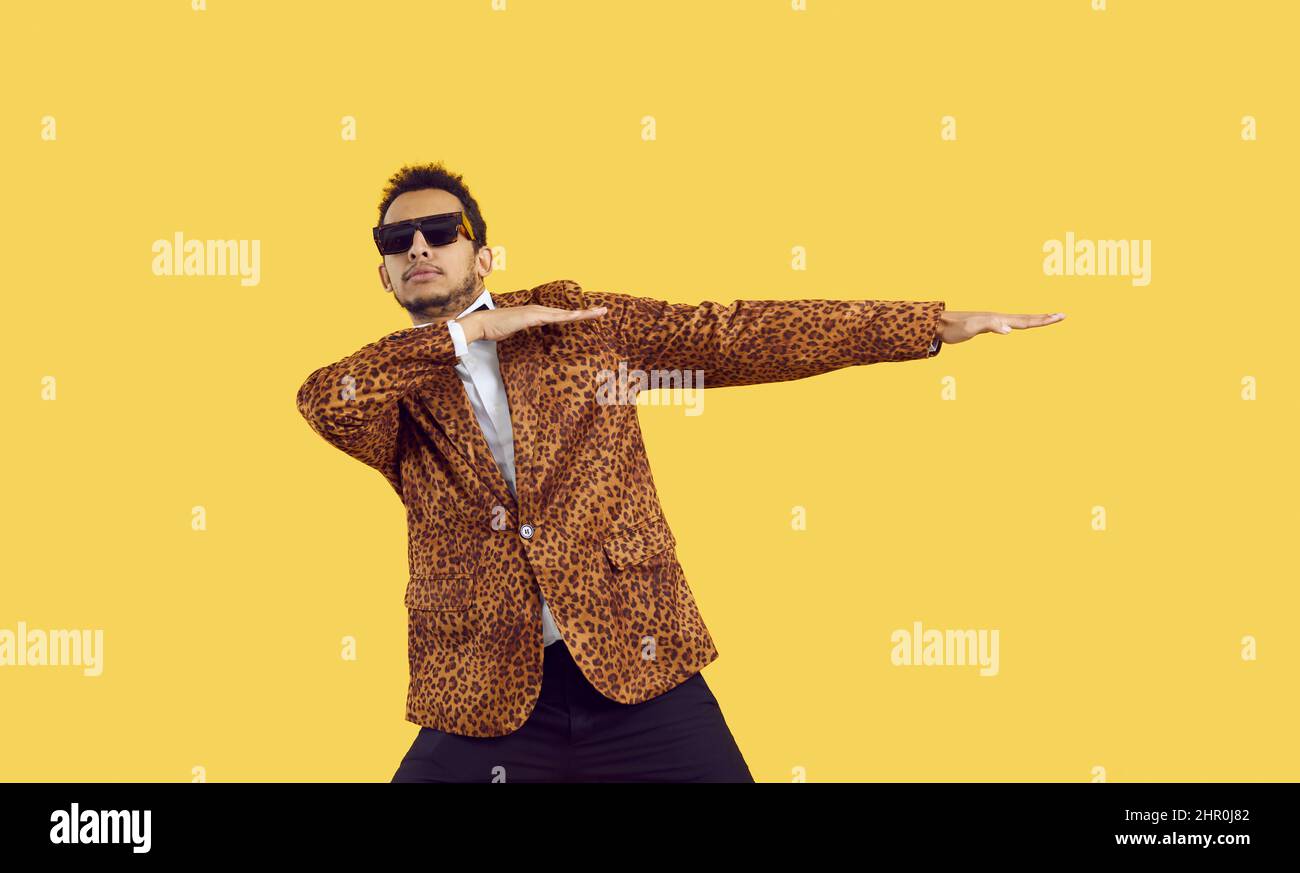 Funny black guy in a leopard jacket and cool glasses dancing isolated on a yellow background Stock Photo