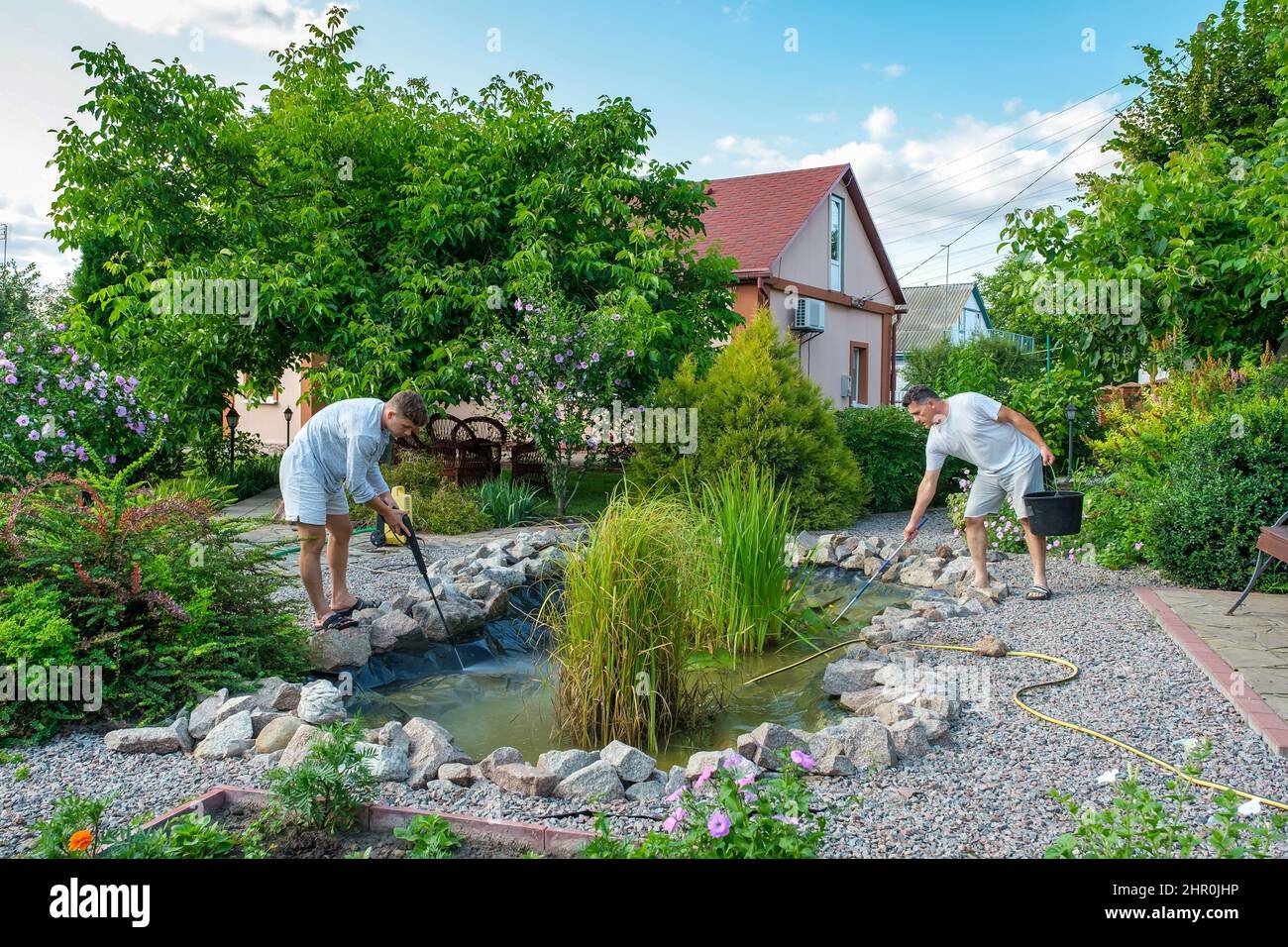 Father and son cleaning garden pond bottom with highpressure washer